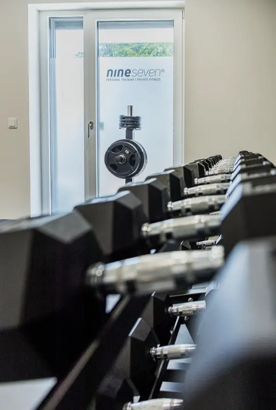 Das hochformatige Bild zeigt das nineseven Fitnessstudio im Medical Center Windmühle in Unterpleichfeld. Die stilvolle und gut ausgestattete Trainingsfläche bietet eine Vielzahl an hochwertigen Fitnessgeräten für ein effektives Workout. Mit einem einladenden Ambiente und professioneller Ausstattung schafft das Studio eine motivierende Umgebung für Fitnessbegeisterte.